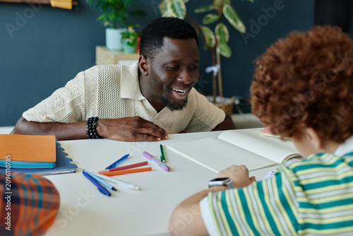Cuadro en lienzo Medium shot of Black male teacher guiding schoolboy during writing practice at desk, supporting literacy and learning