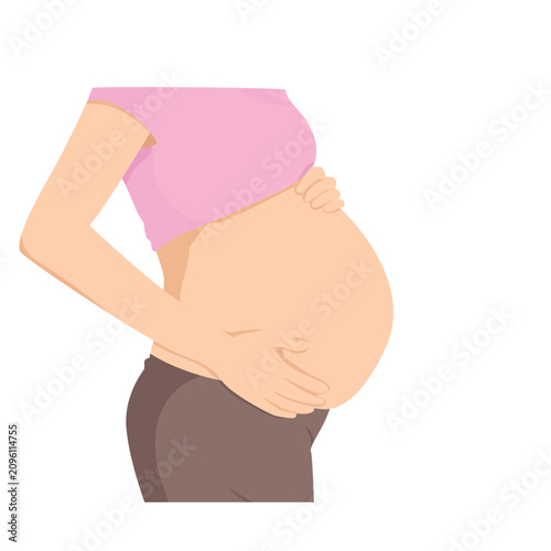 Pregnant woman holds her baby bump with both hands while wearing a pink top and dark brown trousers.