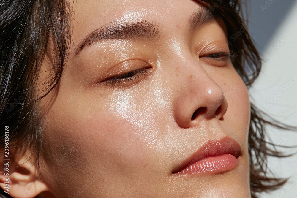 Fototapeta premium Glowing natural skin close up portrait of Asian woman with freckles and minimal makeup, serene expression and soft sunlight highlighting dewy texture