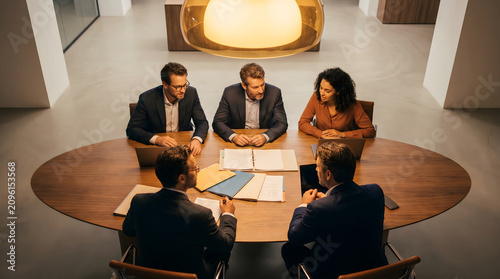 Five business professionals engaged in a serious meeting around a modern oval conference table