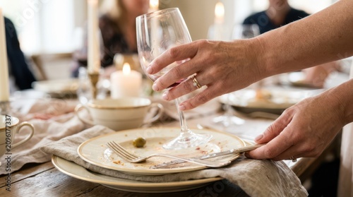 Hands picking up an empty crystal wine glass and a dirty plate from a romantically lit table after an anniversary dinner date.