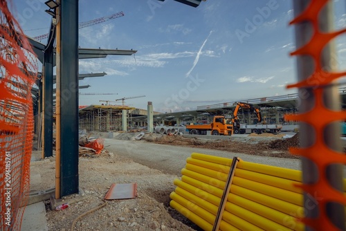 A massive construction zone highlights the major renovation of the Ljubljana train station. Towering cranes, extensive scaffolding, concrete support pillars, and piles of gravel frame
