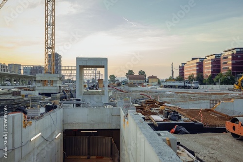 A massive construction zone highlights the major renovation of the Ljubljana train station. Towering cranes, extensive scaffolding, concrete support pillars, and piles of gravel frame 