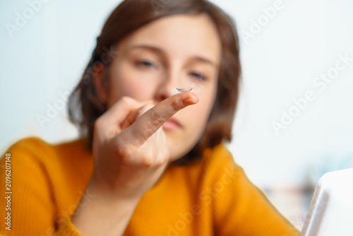 Canvastavla young woman wearing a yellow sweater holding a transparent contact lens on her f