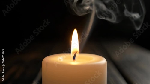 Candle burning slowly on a dark background with smoke rising up in the air