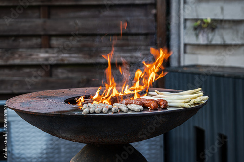 Fotografie Grilling variety of sausages and white asparagus on open fire bowl grill