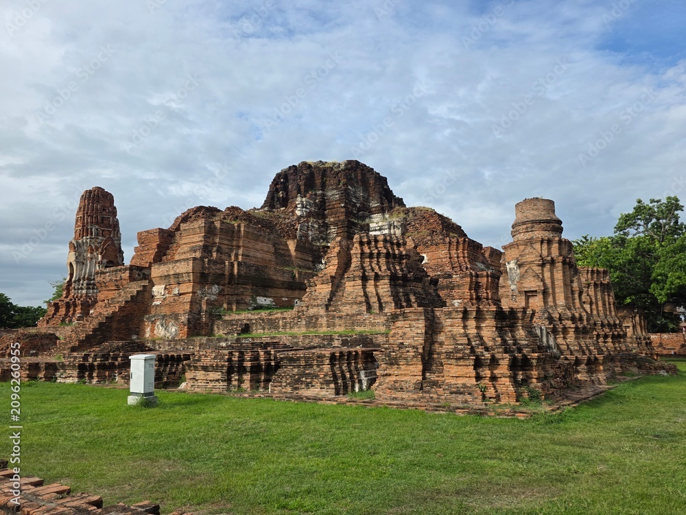 Fototapeta premium Ancient Ayutthaya Ruins: Majestic brick ruins of an ancient temple stand weathered against a cloudy sky, remnants of a bygone era hinting at stories of history and devotion.