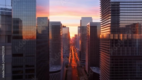 Vibrant sunset over a modern city skyline with gleaming glass skyscrapers and a long urban street stretching into the distance.