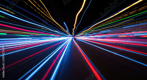 A long, dark tunnel is filled with streaks of vibrant, multicolored light. The lights appear to be moving rapidly, creating a sense of speed and motion.