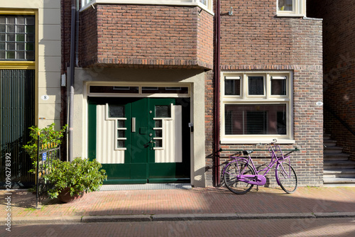 Tablou pe pânză Grünes Tor und violettes Fahrrad an Hausfassade in Groningen, Niederlande