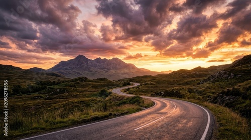 A winding road snakes through a lush, green valley towards a majestic mountain range.