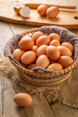 Bild auf Leinwand Basket full of fresh brown eggs on a rustic wooden table with a whisk and shell