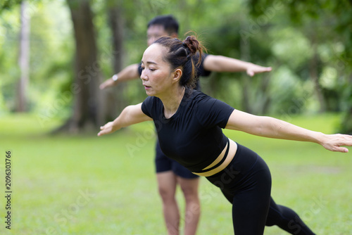 Asian people practicing yoga warrior pose outdoors with a group of friends, fitness and wellness in a peaceful park.