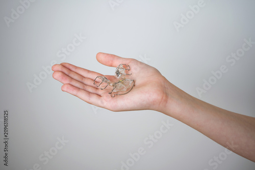 Orthodontic retainer plate lying on a child's open palm. Close up of a child's open hand showing a removable dental plate with metal wires on a neutral light background.