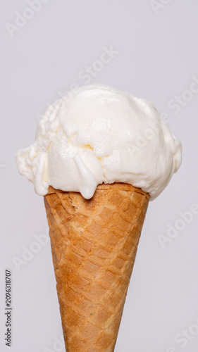 Close-up of single scoop of vanilla ice cream in crispy waffle cone isolated on white background.