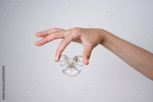 Child holding a removable orthodontic retainer plate on a white background. A close up of a child's hand holding a removable clear plastic orthodontic retainer plate with metal wires