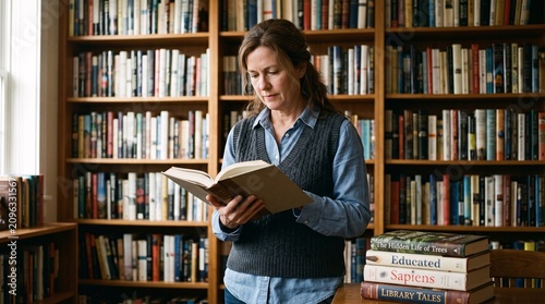 Adult woman peacefully reading a book in a traditional library, surrounded by bookshelves.