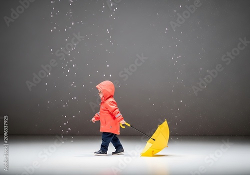 Little child in raincoat dragging yellow umbrella