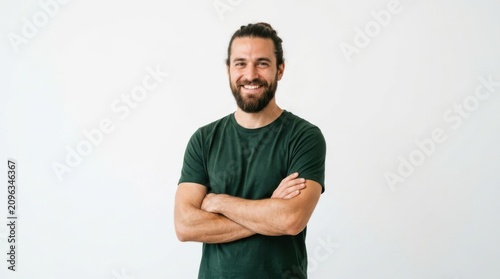 Happy young man with a beard wearing a green t-shirt smiling at the camera with his arms crossed in a casual pose