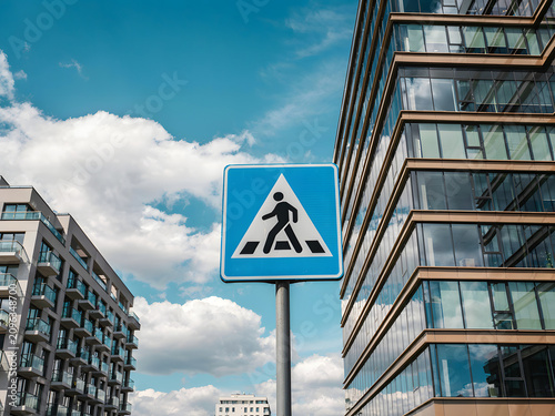 Pedestrian crossing sign in city with modern buildings and blue sky