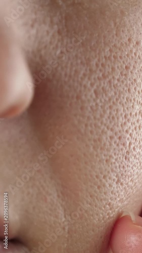 Macro close-up of woman facial skin with visible pores as fingers gently touch the cheek. Vertical video highlights natural skin texture, pore care and realistic beauty without retouching.