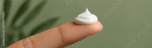 Cream droplet on fingertip with blurred green background