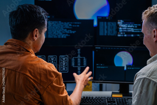 Fotografie A focused dark-haired cybersecurity analyst leans over the workstation studying the screen inside a dark security operations centre at night, defending the corporate network