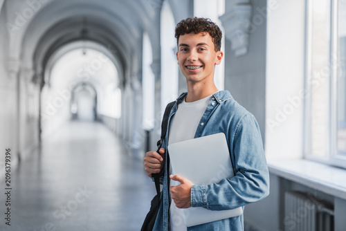 Teenage male student standing in hallway with backpack and laptop, schoolboy portrait, modern education, digital learning and academic life concept