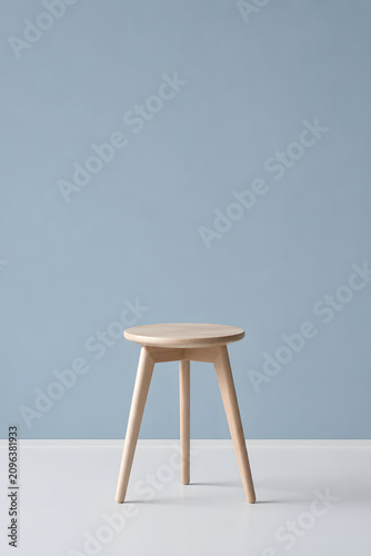 Light wooden three legged stool against soft blue wall minimal interior