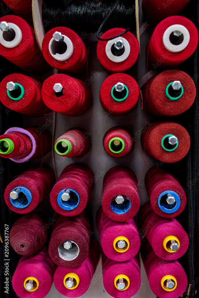 Fototapeta premium Rows of red and pink thread spools fill the frame, showing a bold pattern of sewing supplies with colorful accent centers