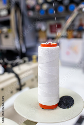 Cuadro en lienzo White thread spool on red base with industrial sewing machine blurred in backgro