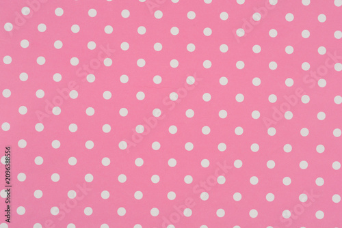 A full frame background texture shows a seamless and sweet pattern of small white polka dots evenly distributed across a pink paper surface.