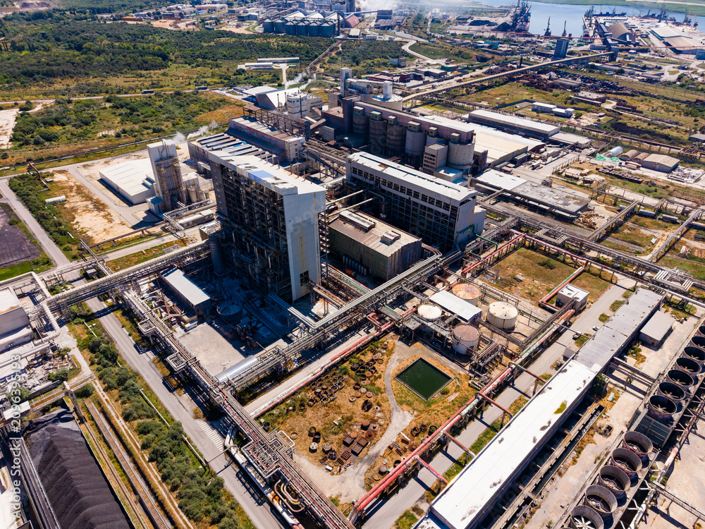 Fototapeta premium Large industrial complex located near a river with multiple storage tanks and pipelines visible during daylight hours