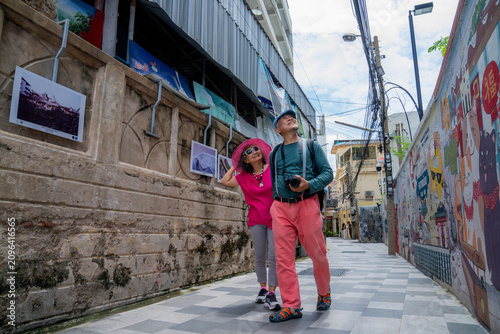 People walking in a colorful alley with street art and photos hanging on the walls during a sunny day