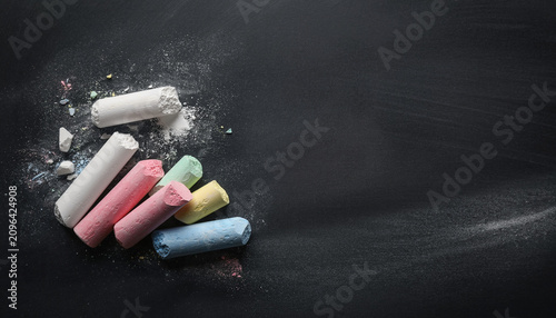 Colorful broken chalk sticks and dust scattered on a blank dark chalkboard background