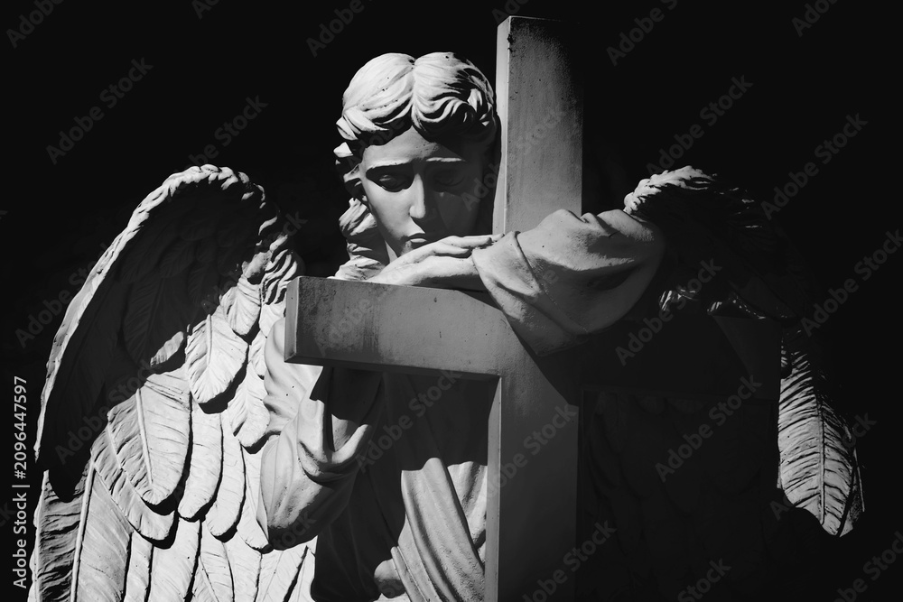 Fototapeta premium Black and white cemetery angel embracing a cross in silent prayer. Symbol of faith, remembrance, hope, eternal peace and divine protection.