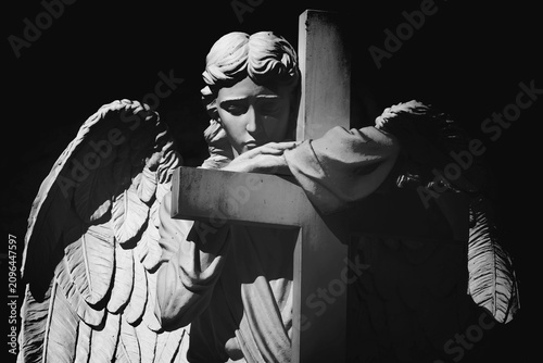 Obraz na płótnie Black and white cemetery angel embracing a cross in silent prayer
