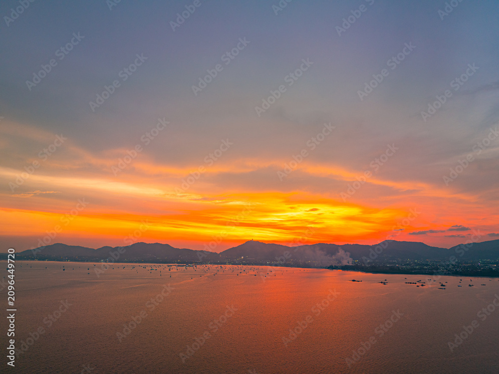 Obraz premium Beautiful golden hour drone image showcasing Phuket's coastal scenery, tranquil ocean, distant mountains, and breathtaking sunset over the tropical island.