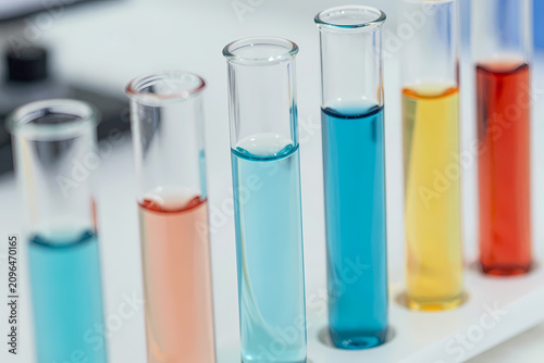 Several glass test tubes filled with colorful chemical liquids stand in a laboratory rack.