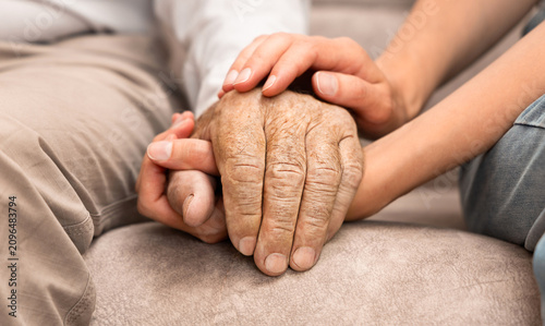 A young woman's hands comfort a senior adult man while sitting on a sofa. Concept of Caregiver Support and Home Care