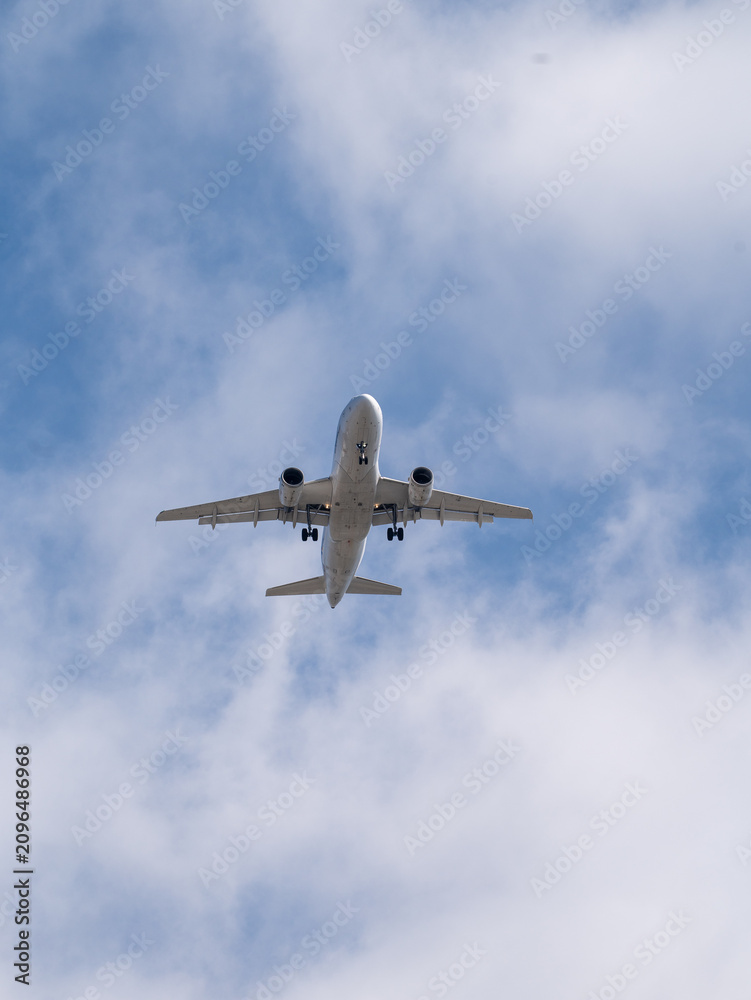 Fototapeta premium Commercial Passenger Airplane Flying Overhead Against Blue Sky During Landing Approach