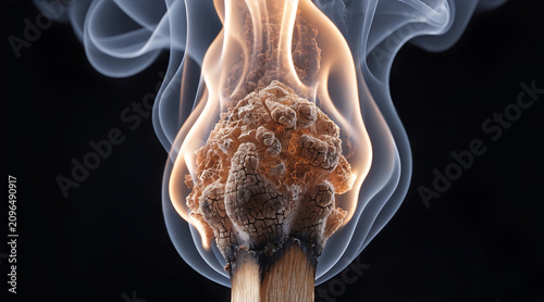 Burning match head with smoke, macro view of flame and charred wood, isolated on black background