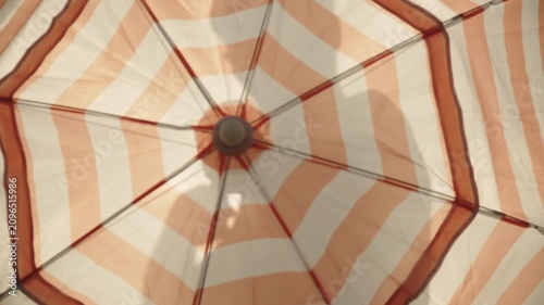Caucasian man opens beach umbrella in front of him on camera against sky. Closeup of striped canopy of protective UV umbrella rotates and silhouette of man inside it.