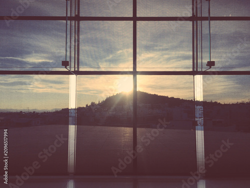 Slika na platnu A serene sunset view through a large window, showcasing a silhouetted hill against a vibrant sky