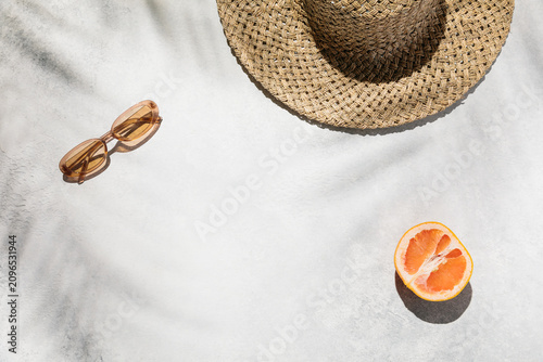 Summer flat lay with a straw hat, sunglasses, and fresh grapefruit on a sunny surface with palm shadows, tropical vacation vibe, healthy beach lifestyle, paradise getaway.