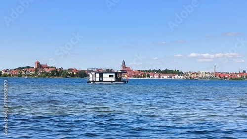 Modern houseboat cruising on a wide lake with a historic European town skyline in the background