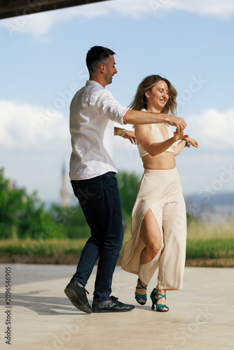 Couple dancing outdoors in casual summer clothing as the woman twirls in a beige skirt while the man leads