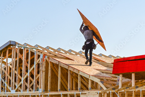 Foto Construction worker carrying an OSB roof sheathing panel on the roof of a two st