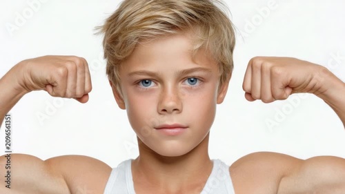 Young boy shows strong muscles and confidence in front of a white background during a bright and sunny day