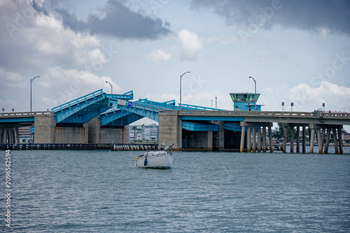 Cuadro en lienzo Blue bascule drawbridge raised above a calm harbor as a motorboat and sailboat pass beneath in St